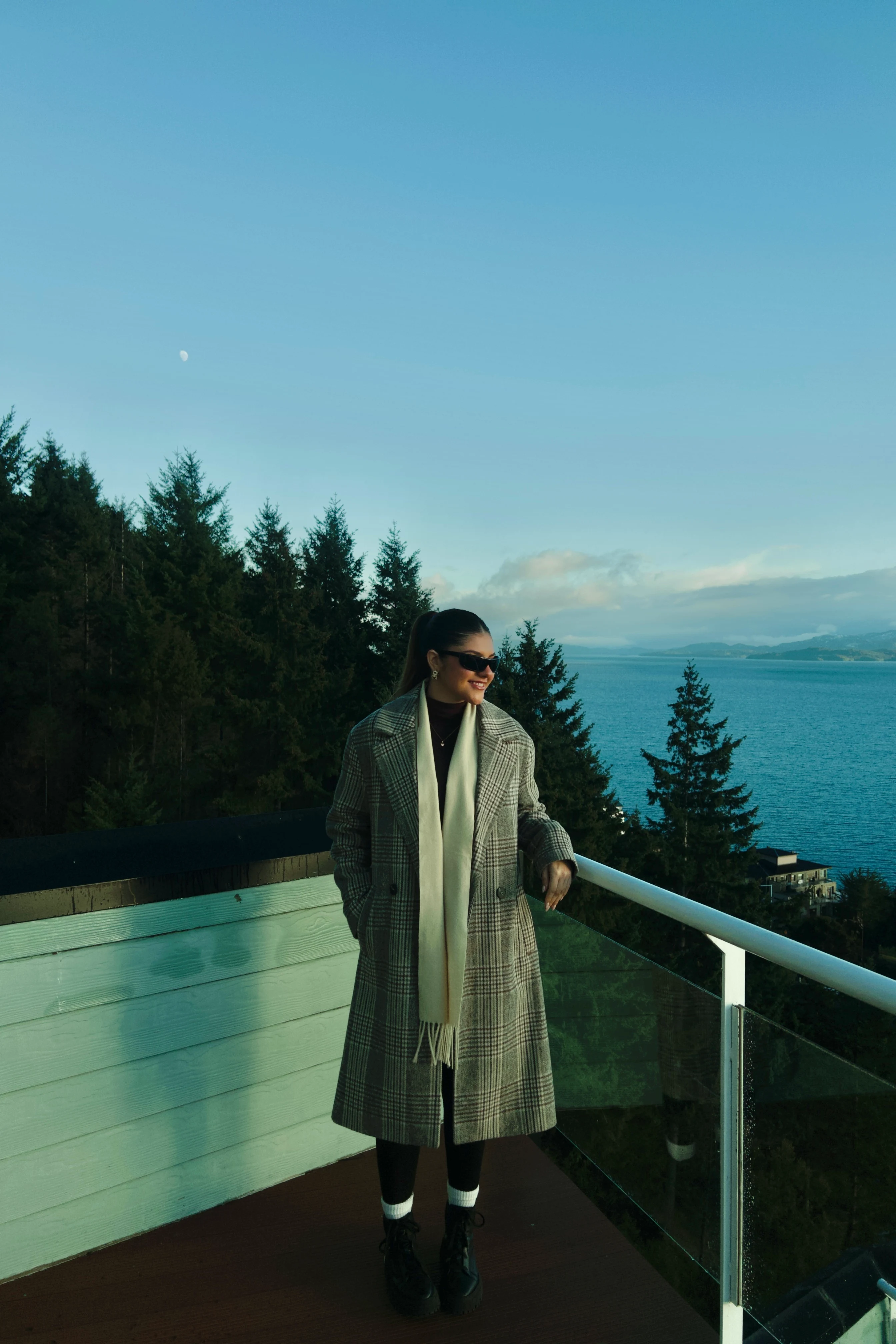 Sol Poretti em sacada alpina de madeira com vista para o lago Nahuel Huapi na Patagônia, com casaco elegante e expressão tranquila.